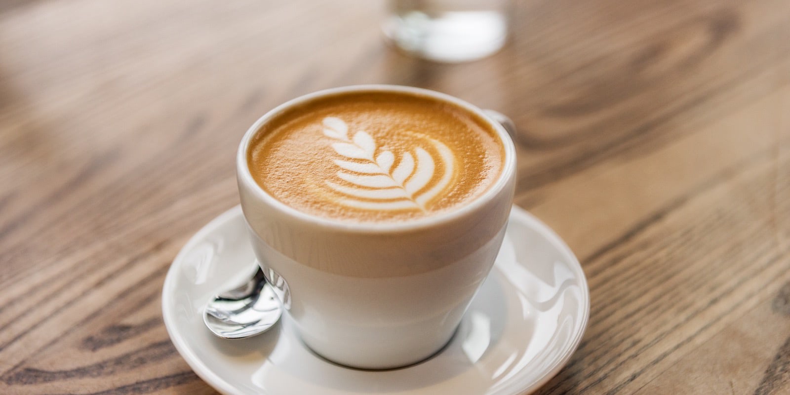 A café latte with leaf-patterned foam served on a wooden table