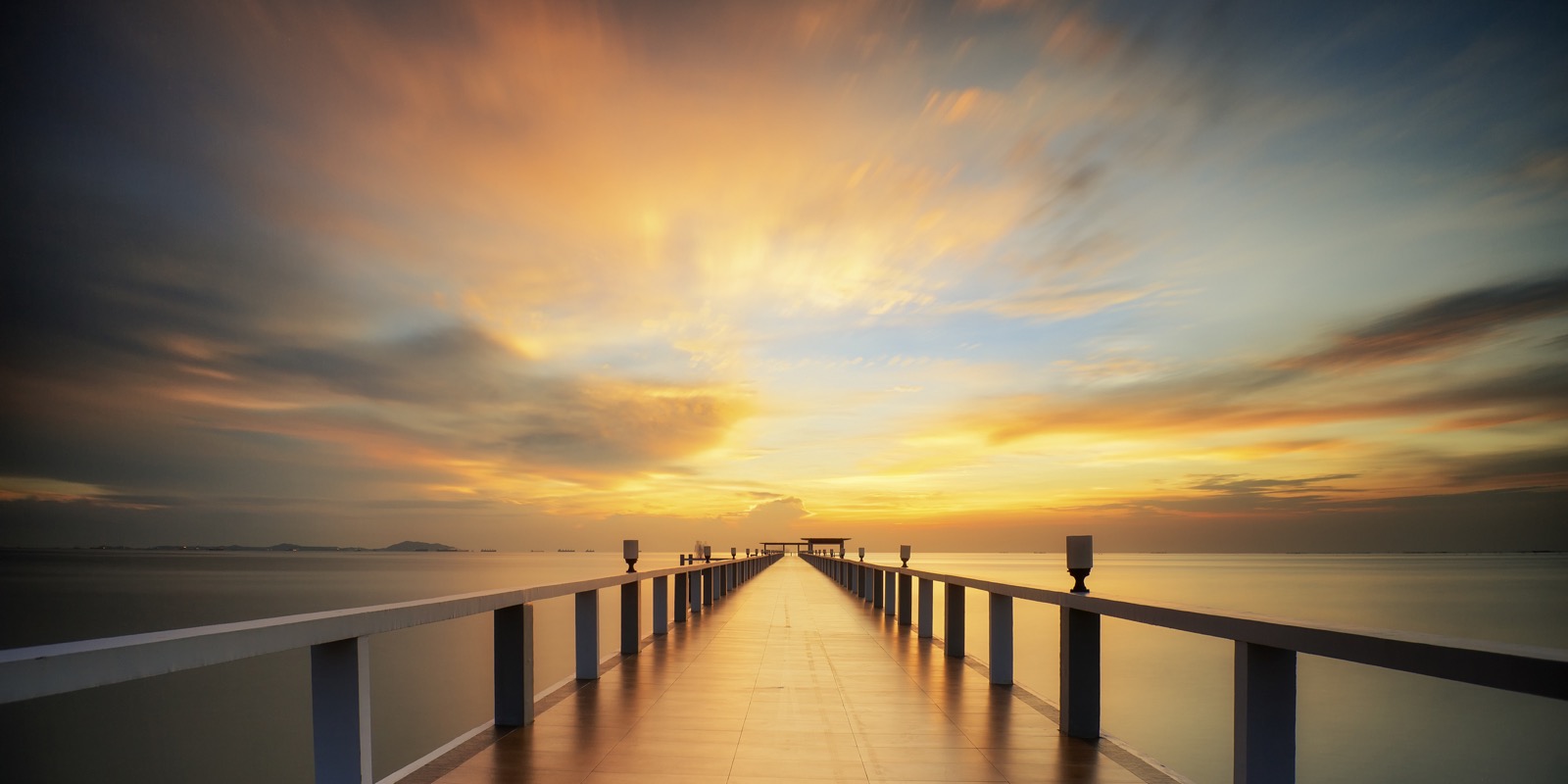 A straight pier leading across calm water toward a bright horizon.