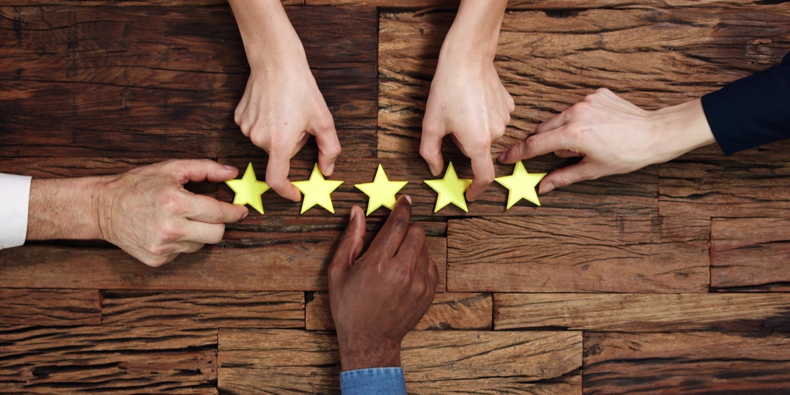 Hands arranging five yellow rating stars on a wooden table.