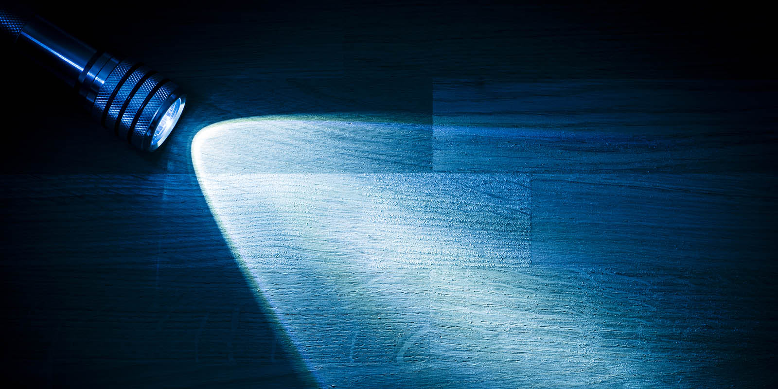 A flashlight casting a narrow beam across a dark wooden surface, representing competitor research