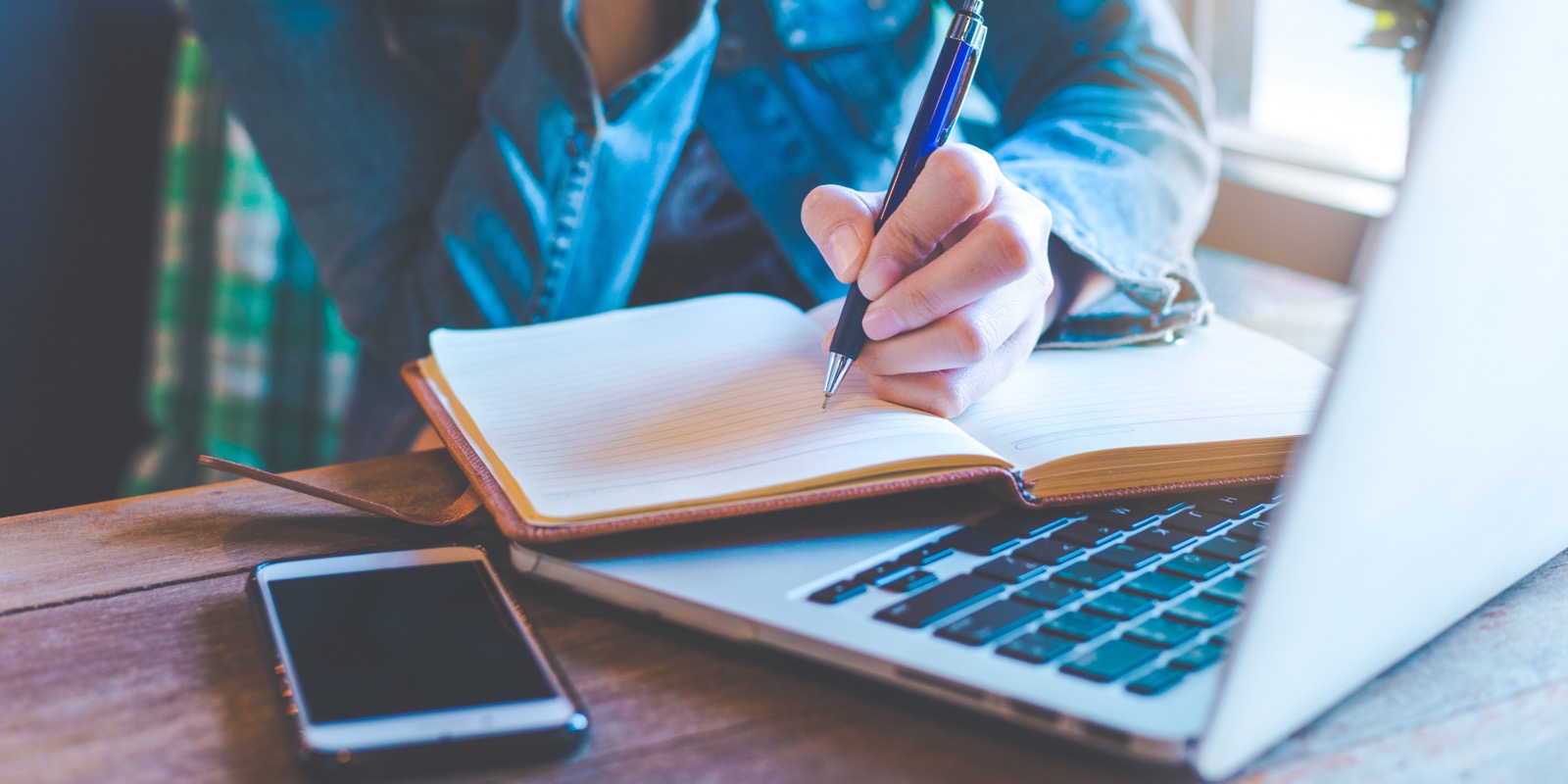 Writer taking notes beside a laptop and phone